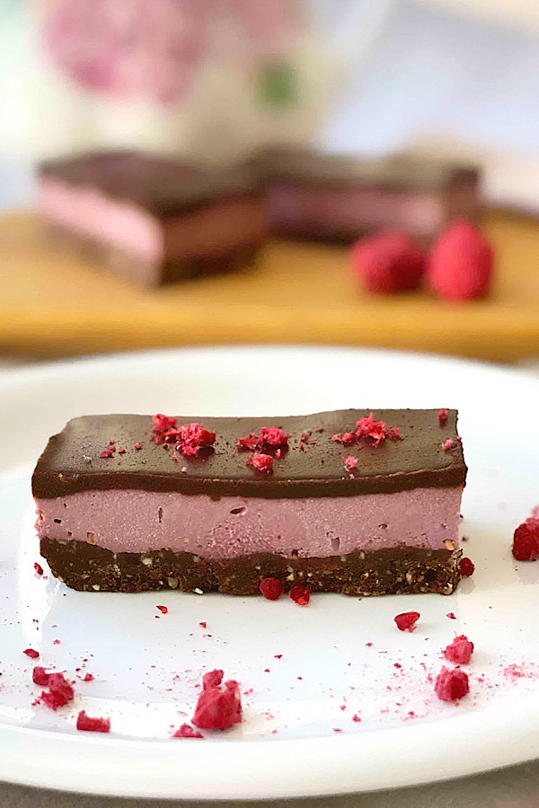 Close up of Raw Raspberry Choolate Slice on a plate with freeze-dried raspberries scattered over the top.
