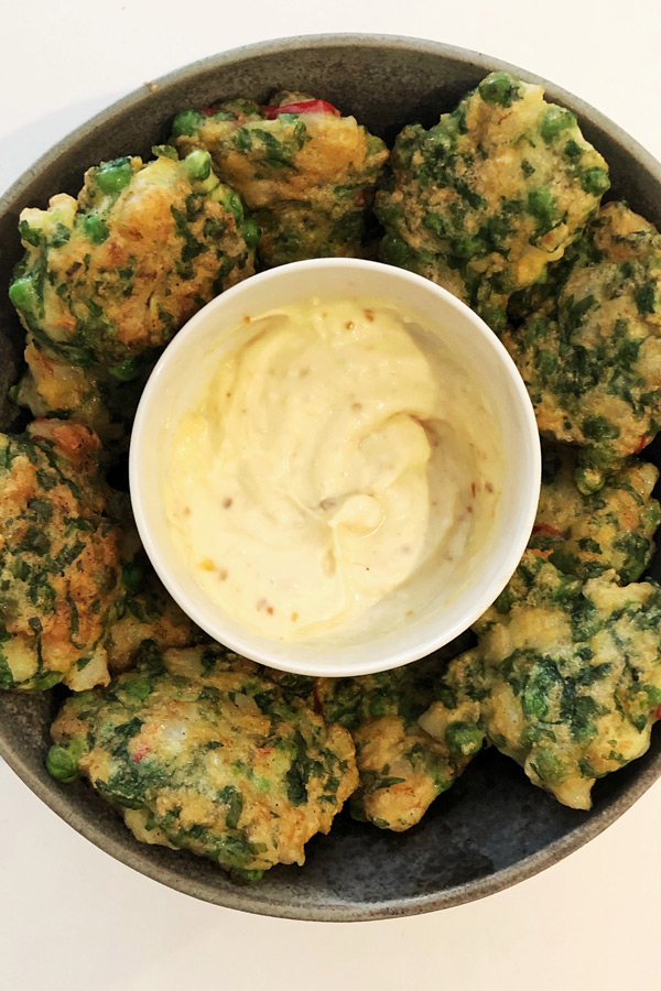 Looking down on a plate of Prawn, Pea and Coriander Fritters with a bowl of aioli in the centre.