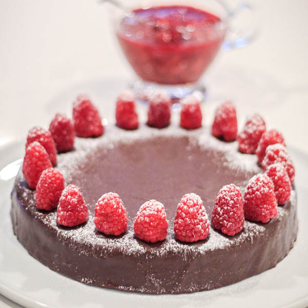 Torta with raspberry couli in a jug in background.