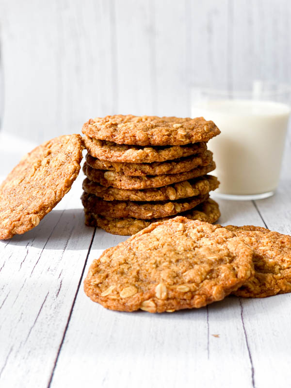 Close up of a stack of Anzac Biscuits with a glass of milk in the background.