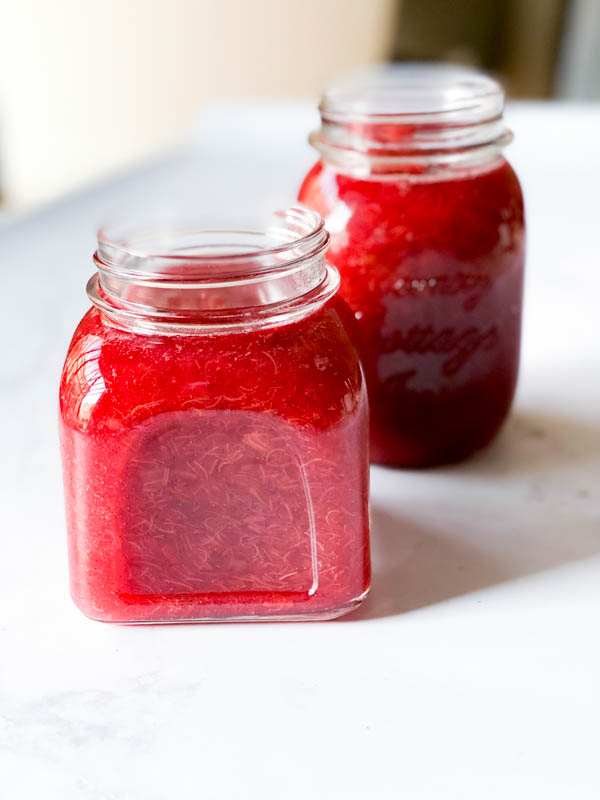 2 jars of Easy Rhubarb Compote with lids off, cooling on a marble bench