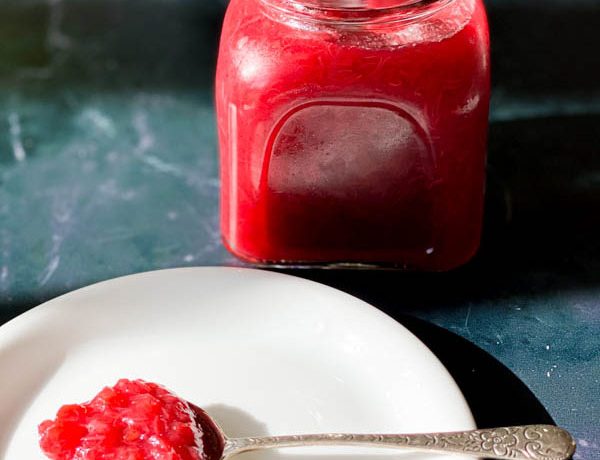 Close up of a jar of Easy Rhubarb Compote and in front of it is a white plate and spoon which has rhubarb compote on the spoon.