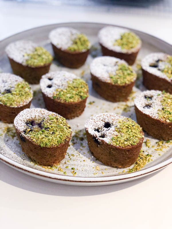 Pistachio Blueberry Friands topped with crushed pistachios and icing sugar on a pottery platter.