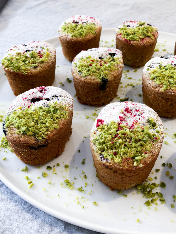 Close up of Pistachio Blueberry Friands decorated with crushed Pistachios on one half and Icing sugar on the other half.