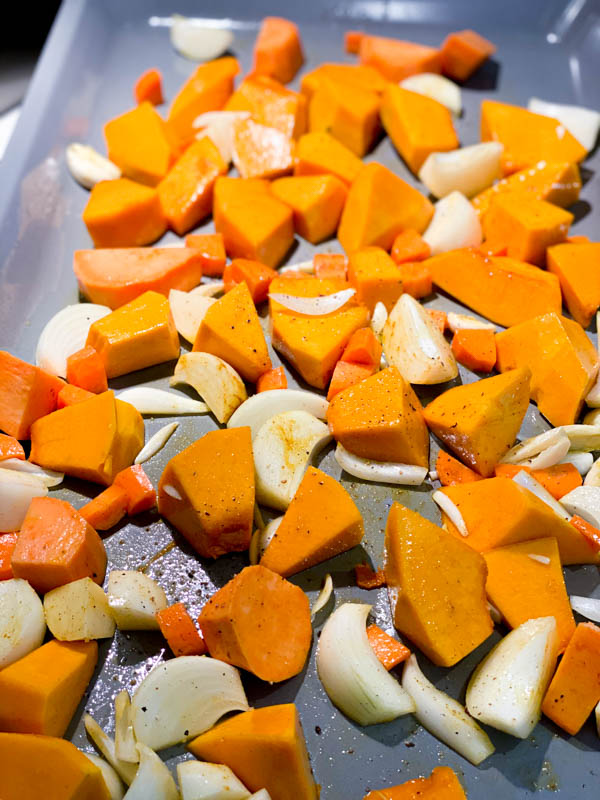 raw pumpkin and potato pieces, carrot, onion and garlic seasoned with salt, pepper, curry powder and olive oil on an oven tray ready to go into the oven.