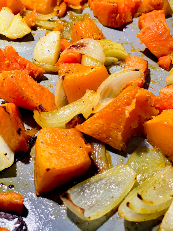 Close up of roasted pumpkin and potato pieces, onion, garlic, carrot and sweet potato roasted on an oven tray, ready to be blended into soup.