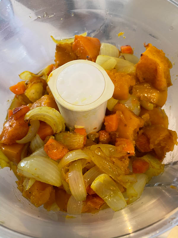 All the roasted vegetables in the bowl of a food processor, ready to be blended.