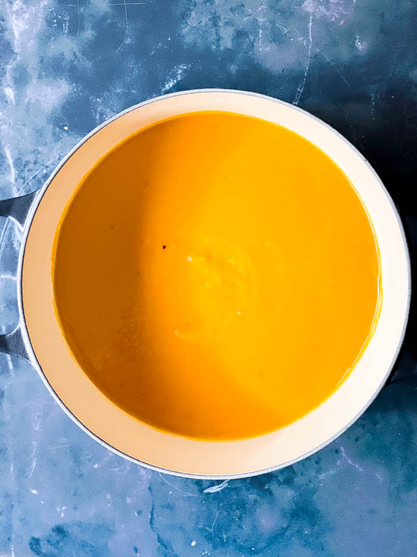 Looking down into Roasted Pumpkin Soup in a pot on a dark marble bench top.