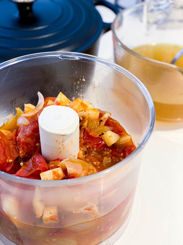 Roasted tomato mixture in the bowl of food processor ready for pureeing.