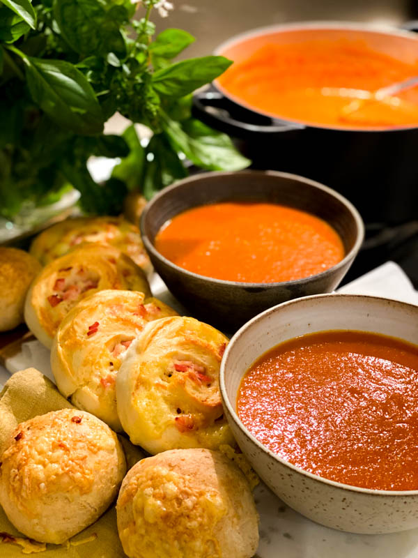 Roasted Tomato Soup in 2 bowls with bread rolls and scrolls ready for serving.