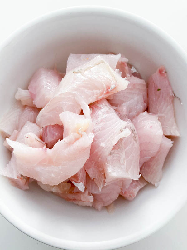 White fish fillets chopped into pieces in a white bowl.