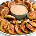 Close up of Thai Fish Cakes on a large round platter with a bowl of Sweet Chilli Mayo in the middle.