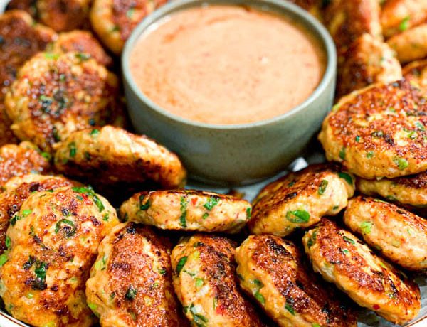 Close up of Thai Fish Cakes on a large round platter with a bowl of Sweet Chilli Mayo in the middle.