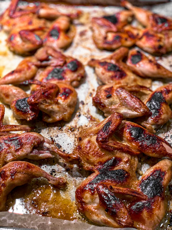The butterflied Quail on a baking paper lined baking tray, once it has cooked. The skin is beautifully charred and browned.
