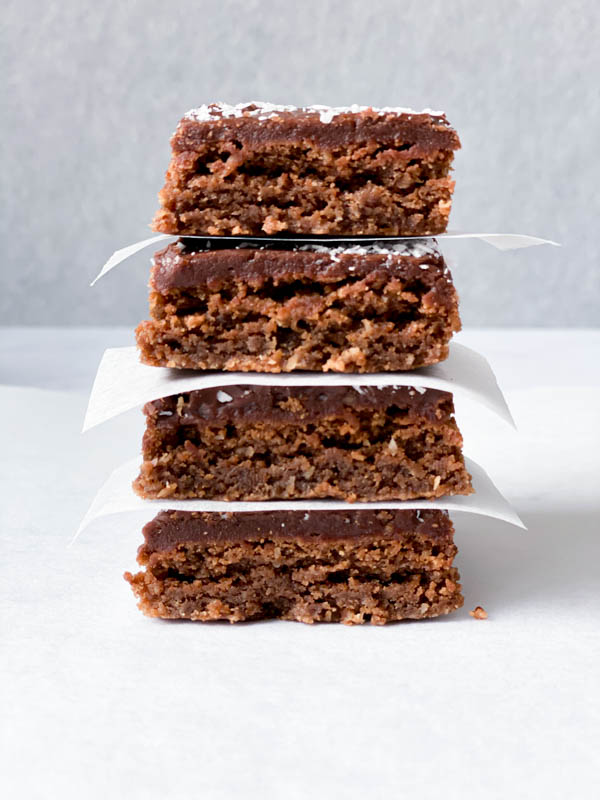 A stack of 4 Chewy Chocolate Coconut Slices with white baking paper in between each slice.