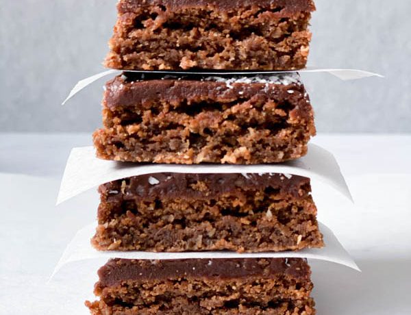 Close up of a stack of 4 Chewy Chocolate Coconut Slices with white baking paper in between.