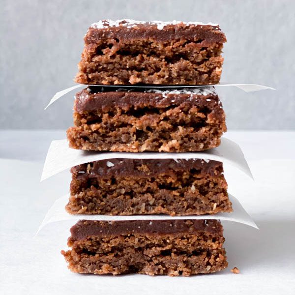 Close up of a stack of 4 Chewy Chocolate Coconut Slices with white baking paper in between.