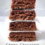 A stack of 4 Chewy Chocolate Coconut Sices with white baking paper in between with a grey background.