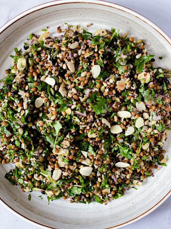 Looking down onto a large white ceramic platter with the Cypriot Grain Salad spread out on it.