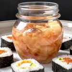 An open jar of Easy Pickled Ginger on a white platter surrounded by pieces of sushi rolls.