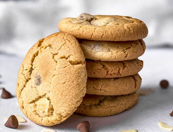 Close up of 5 stacked Gingernut Biscuits with one leaning against them. In the foreground are almond flakes and milk chocolate nibs.