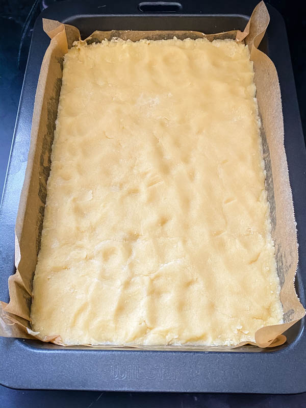 The shortcrust base for the Gooey Yuzu Slice pressed into the bottom of a slice tin to form the first layer.