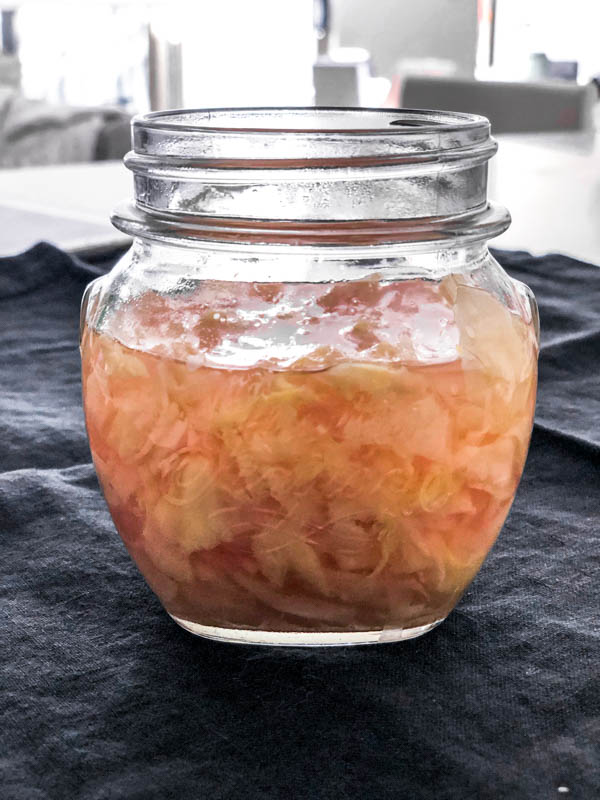 A jar of Easy Pickled Ginger on a slate napkin and the lid is off the jar.
