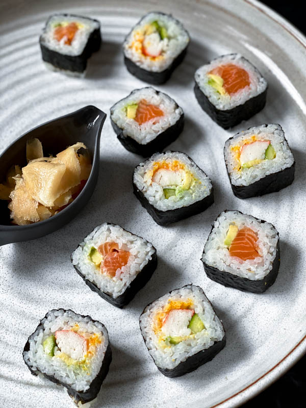 Looking down onto a white pottery round large platter which has sushi rolls on it with a small oval dish of Easy Pickled Ginger in the middle.