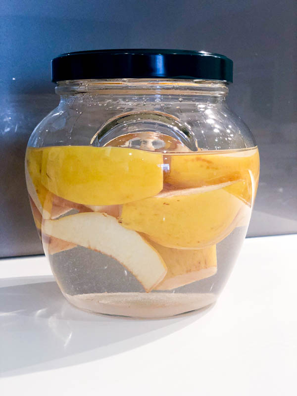 A glass jar filled with Quince, Gin and sugar with a green lid on the jar.