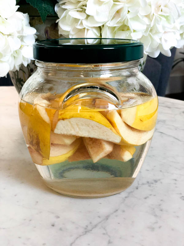 A sealed jar of Quince Infused Gin on top of a marble table with white hydrangea flowers behind it.