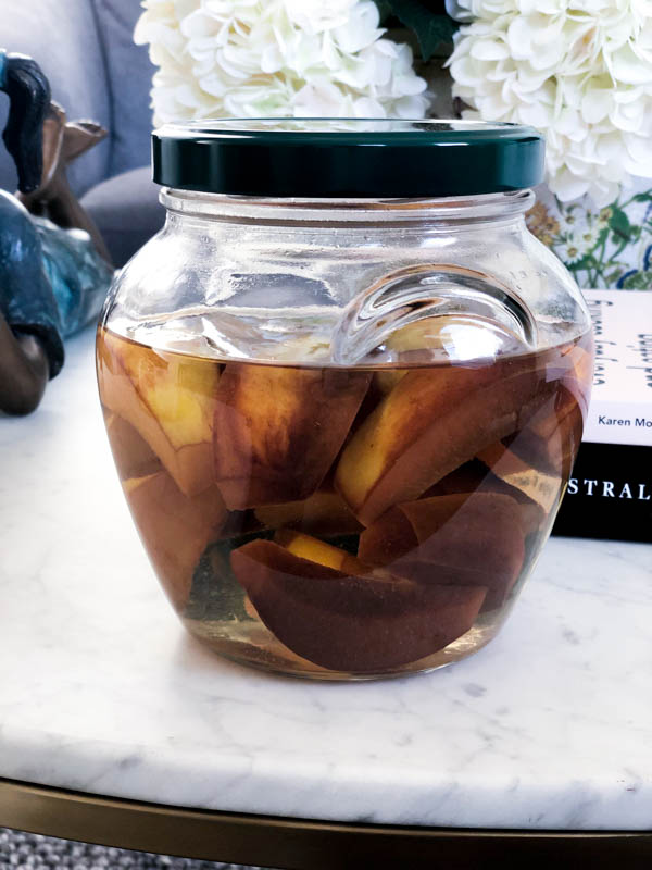 A glass jar of Quince Infused Gin showing the fruit has now changed colour to a dark golden brown after infusing for 4 weeks.