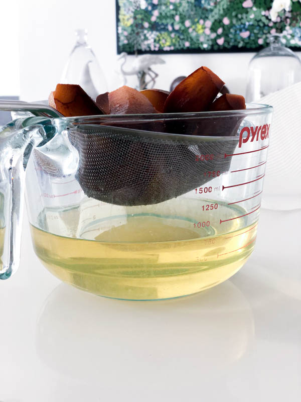 The Quince being drained in a sieve over a large pyrex jug, showing the golden liquid of the Gin in the jug.