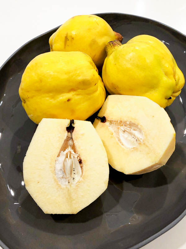 A dark platter of washed yellow Quince Fruit with one cut open to reveal the inside.