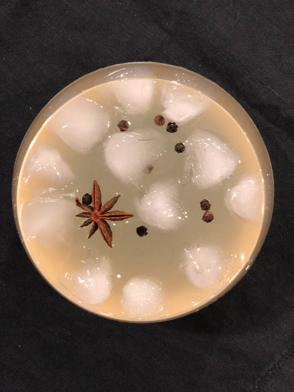 Top view looking down into the glass of Quince Infused Gin and tonic with ice, star anise and black peppercorns as a garnish.