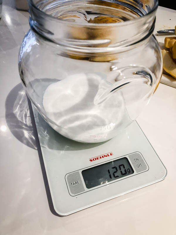 A glass jar with sugar weighed into it on top of kitchen scales showing the measured amount as 120g.