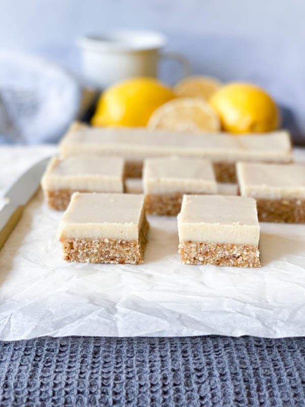 Raw Lemon Slice cut into squares on white baking paper with lemons in the background.