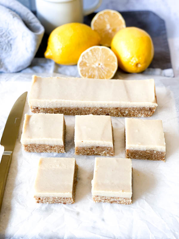 Top view of Raw Lemon Slice with lemons, napkins and a white coffee cup in the background and a gold knife to the left of the slices.