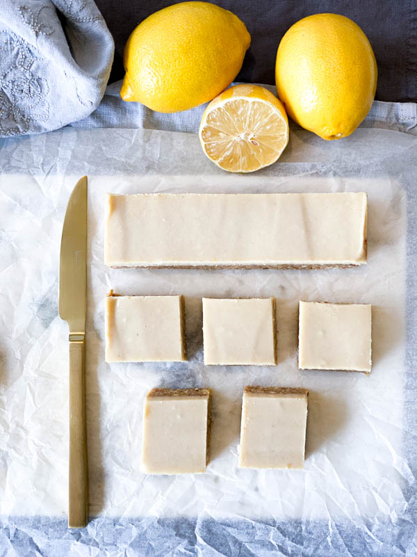Top view of Raw Lemon Slice, some cut into squares and one cut in a row with a gold knife to the left and lemons at top.