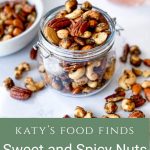 A jar of Sweet and Spicy Nuts in a jar with the lid off. Nuts are also scattered in front of it on a white marble bench. A low white bowl of nuts is to the left of the jar with sprigs of rosemary and a glass of gin in the background.