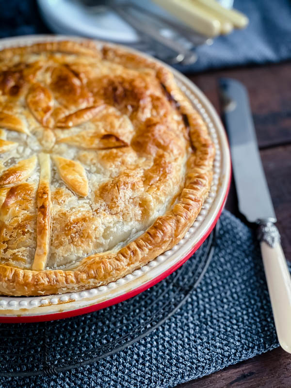 Close up of a Beef and Vegetable Pie which is only half in the photo with a knife next to it.