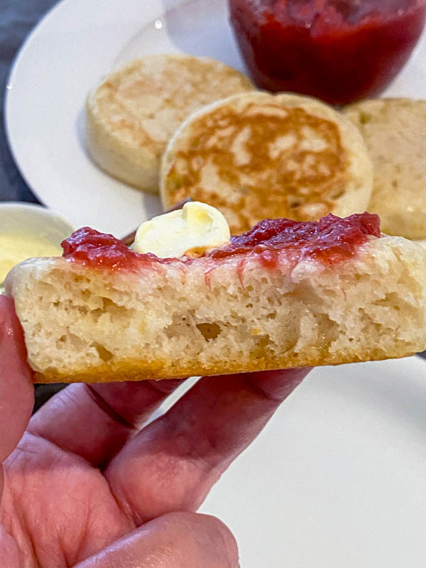 A half eaten Sourdough Crumpet close up showing the holey texture of the inside of the crumpet. In the background are more crumpets on a plate.