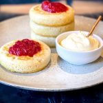 A stack of 3 Sourdough Crumpets with a single crumpet also on the plate in front of them. Next to them is a small bowl of creme fraiche.