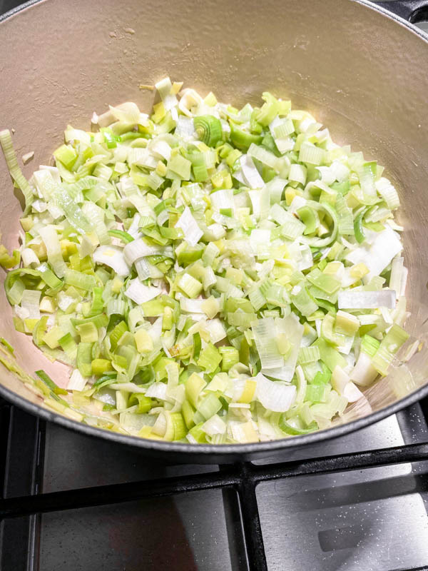 Chopped leeks in a Le Creuset pot being sauteed.