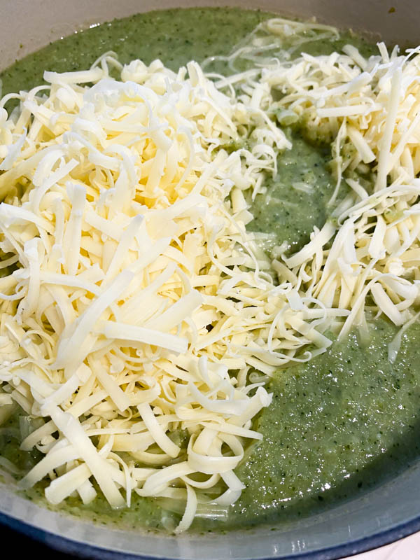 This shows the blended soup back in the cleaned pot with grated cheese on top, ready to be stirred through .