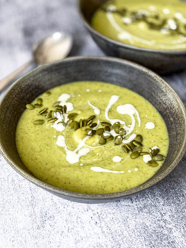Close up of the bowl of Broccoli Soup garnished with pumpkin seeds and a swirl of cream.