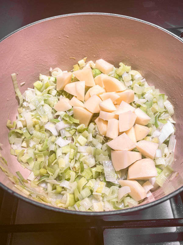 Chopped sauteed leeks in a large Le Creuset pot with chopped potatoes added.