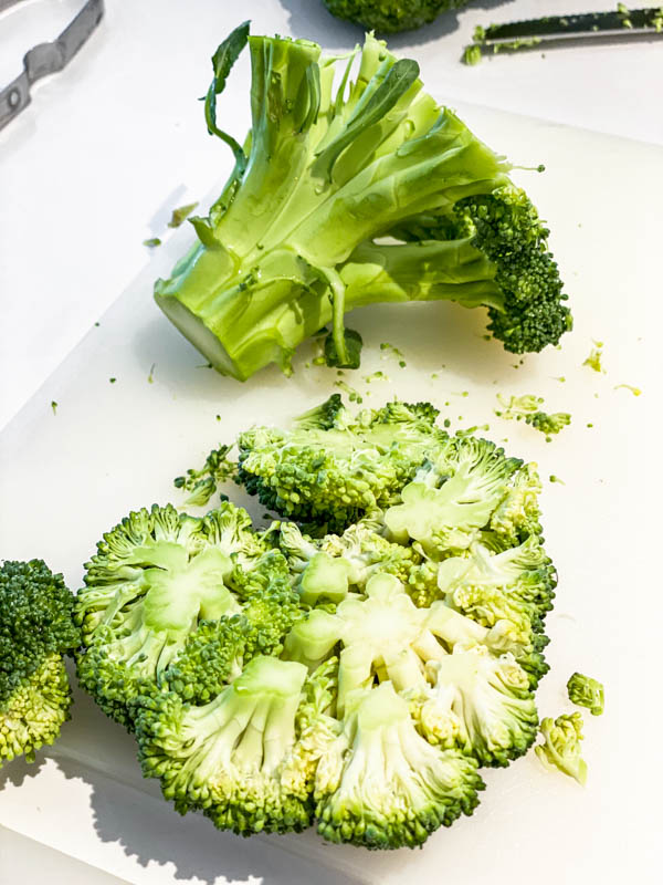 Broccoli head on a white choppng board, showing the top florets cut off as close to the floret as possible, leaving the stalks.