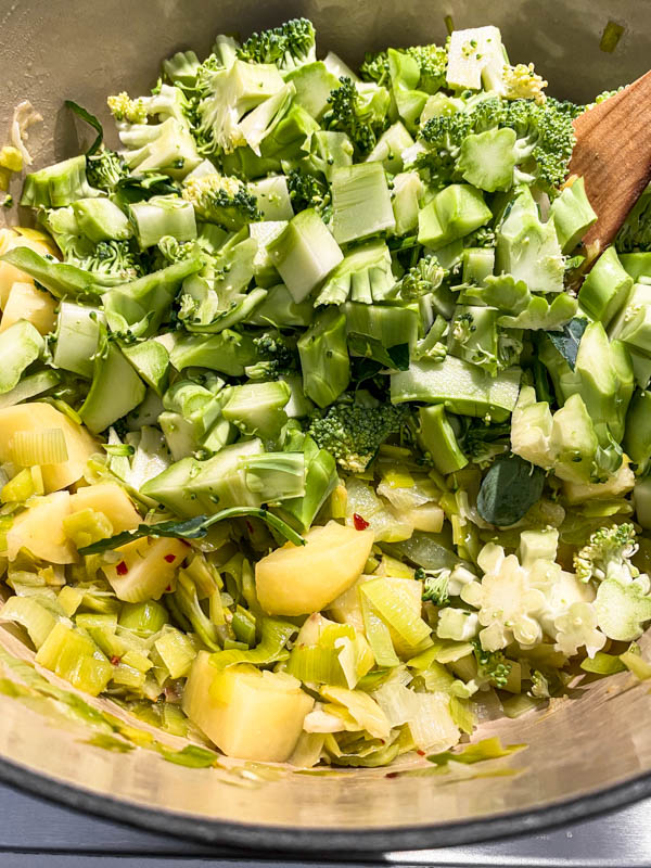 The chopped broccoli stalks are added to the softened leeks and potato in the large pot.