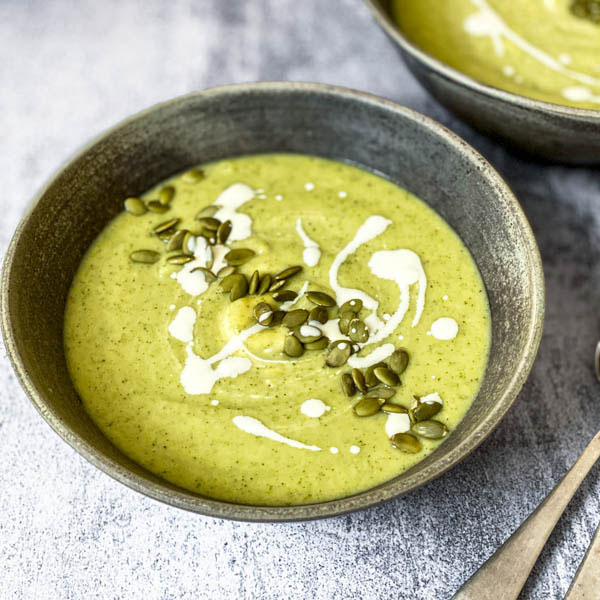 A bowl of Broccoli Soup on a grey bench top with another bowl behind it.