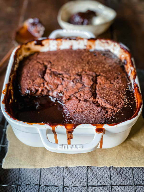 Chocolate Self Saucing Pudding in a square, white ovenproof dish with a spoonful of pudding removed to reveal the soft fudgy sauce in the bottom.
